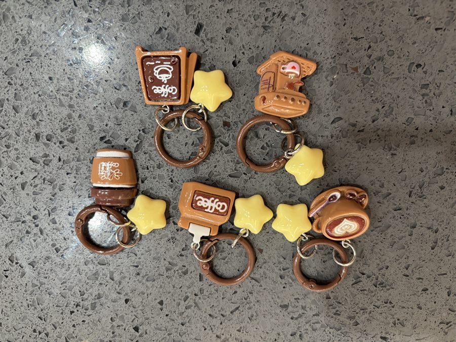 Coffee-themed keychain charms shaped like cups, a espresso machine and a café counter