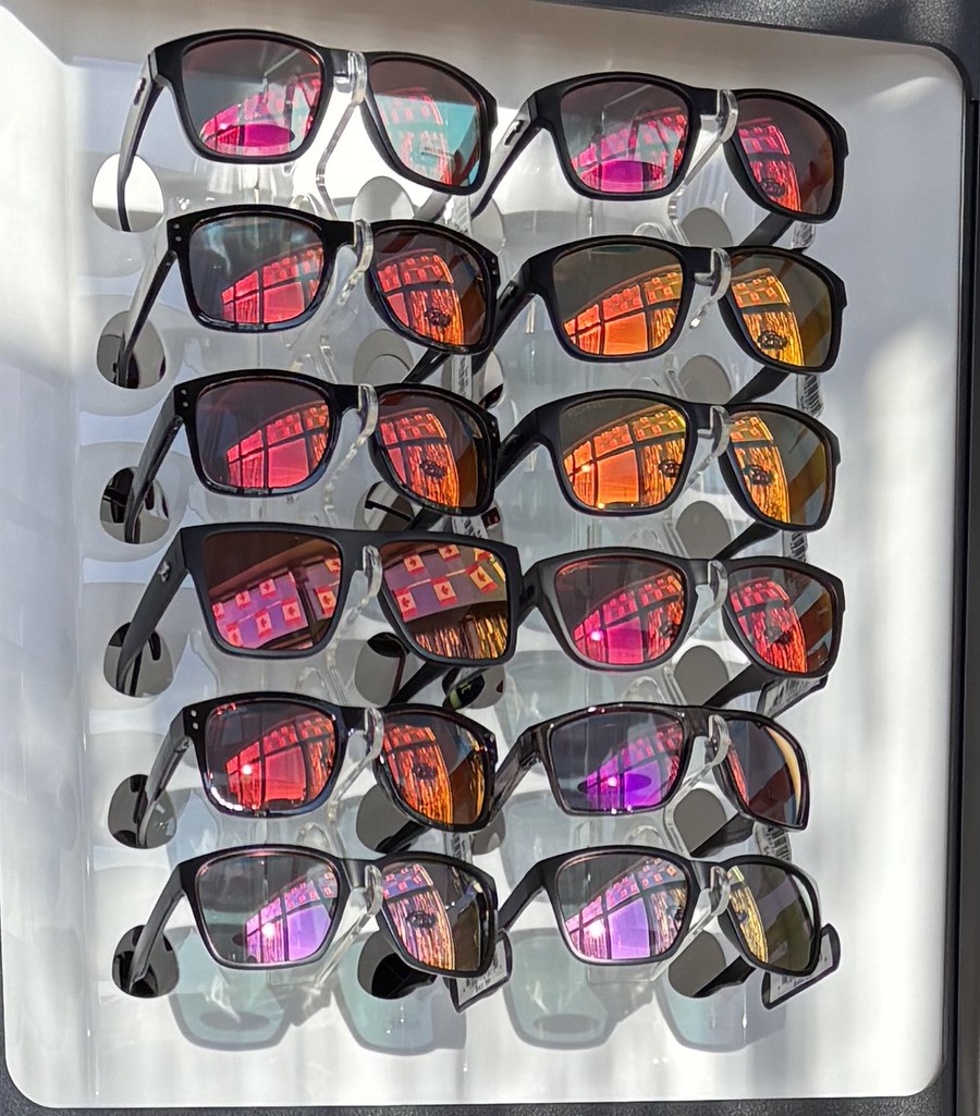 Rows of sunglasses with mirrored pink, orange and purple lenses on a display rack